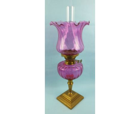 An antique brass oil lamp with cranberry glass shade and reservoir, 58cm high.