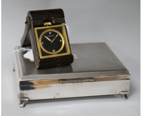 A Doka eight-day military travelling clock and a plated cigarette box, the clock having circular black dial in square brass c