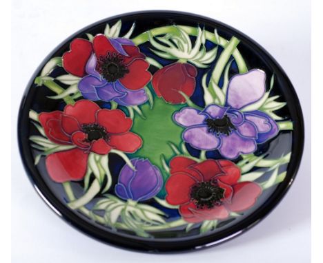 MODERN MOORCROFT 'ANEMONE' PATTERN TUBE LINED POTTERY PLATE, decorated in tones of purple, red, green and black on a dark blu