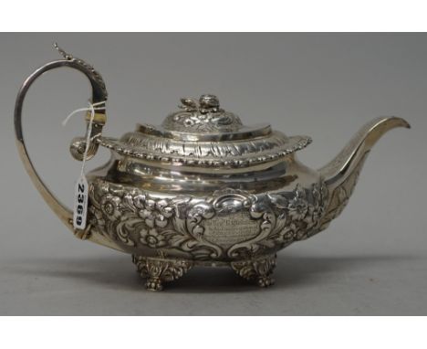 A George IV silver teapot, of compressed oval form, with floral and foliate embossed decoration, the hinged lid with a cast b