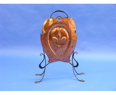 An Arts & Crafts copper shield-shaped Fire Screen, with embossed Fleur-de-Lis decoration on a wrought iron frame, together wi