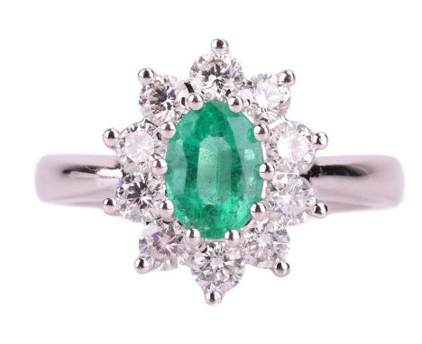 An emerald and diamond cluster ring in 18ct white gold, centred with an oval-cut emerald of 6.8 x 5.2 x 4.3 mm, surrounded by