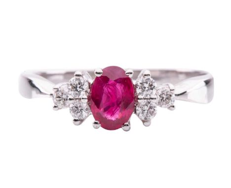 A ruby and diamond ring, centred with an oval-cut ruby of 6.0 x 4.0 x 2.5 mm, flanked by diamond trefoil clusters with an est