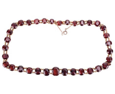 A red garnet rivière necklace in gilt metal, featuring 34 claw set graduated oval-cut red garnets in individual collets linke