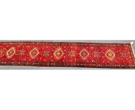 A 20th century North West Persian Heriz runner carpet floor rug. Having a red central field populated with geometric patterni