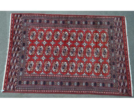 A large mid 20th century Pakistani Persian Bokhara style hand knotted carpet floor rug. The rug having a red ground, with lar