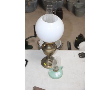 A small brass oil lamp with opaque shade and chimney and a small hand held green reservoir oil lamp
