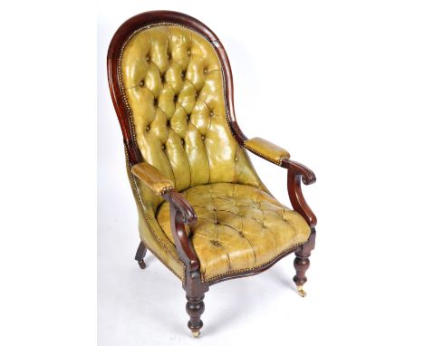 A 19th Century Victorian green leather and mahogany fireside armchair / library chair having a shaped button backrest with le