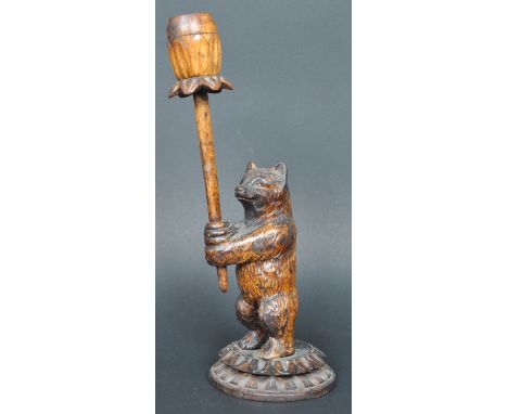 A 19th Century German Black Forest hand carved figural candlestick in the form of a bear having a carved floral candle sconce