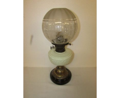 A squat Victorian oil lamp with impressed brass stem on a circular clack ceramic base, with a light green glass reservoir and