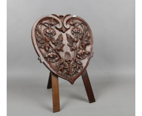 An early to mid 20th century carved oak easel firescreen of heart form decorated with poppies.