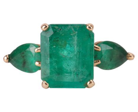 An emerald trilogy ring, centred with a step-cut emerald with canted corners of 9.8 x 8.1 x 5.2 mm, flanked by two pear-cut e