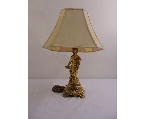 A gilded metal table lamp in the form of a putti on raised circular base with silk shade