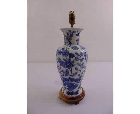 A Chinese blue and white baluster vase lamp stand decorated with floral sprays and leaves, mounted on a circular wooden base