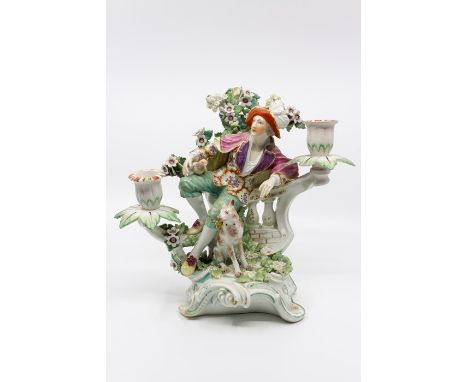 A Derby porcelain figural candleabrum, circa 1760-65 modelled as a man reclining on a balustrade, with dog and boccage, patch