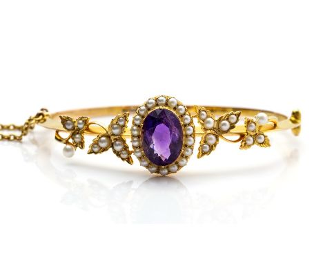 A Victorian amethyst and seed pearl oval cluster hinged yellow gold bangle with seed pearl set applied leaf shoulders, the ce