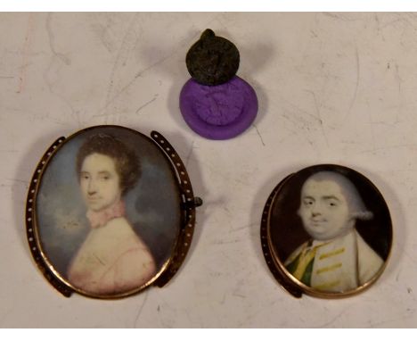 Two George III oval portrait miniatures in buckle mounts, one a gentleman, the other a lady, together with a miniature fob se