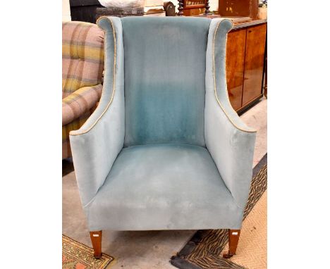 An Edwardian blue upholstered wing back armchair, raised on square tapering legs to ceramic castors