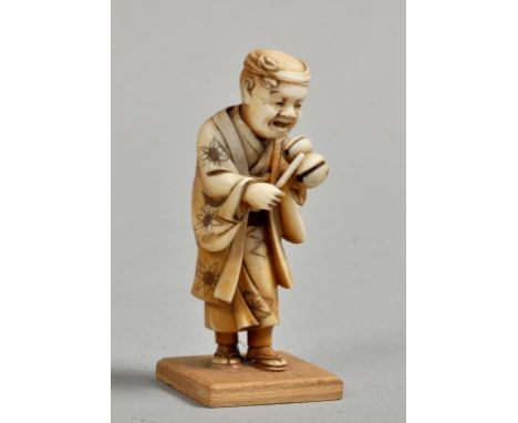 A Japanese Meiji period ivory netsuke in the form of a standing robed gentleman playing a nut instrument and he with a noddin