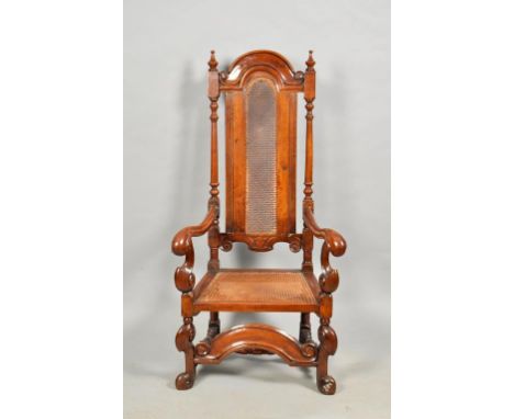 A walnut Carolean style open armchair with caned back panel and seat, carved in the period style.