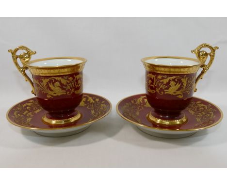 A pair of early 20th century Dresden coffee cups and saucers, with ornate raised gilt decoration on a red ground, the cups wi