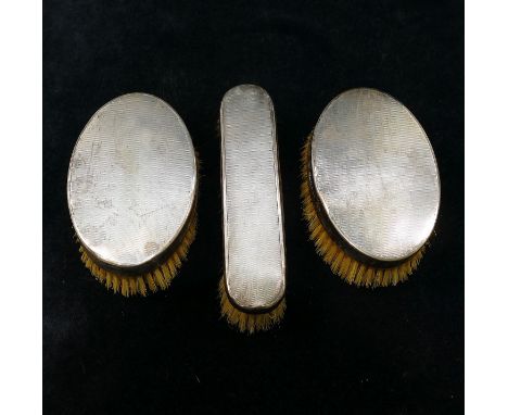 Three silver backed brushes, London 1927, comprised of a pair of oval brushes and one other brush, with engine turned decorat