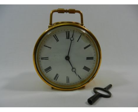 A circular gilt brass cased mantle clock, the white enamel face with Roman numerals, 9cm diameter, with hinged carrying handl