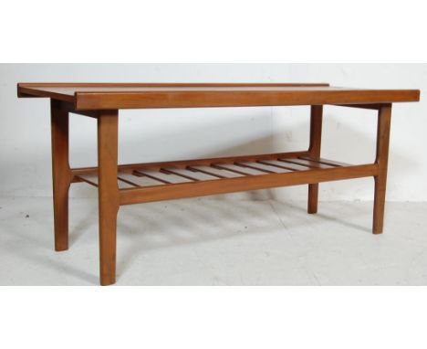 A vintage 1970’s teak wood coffee table of a rectangular form with lipped edges raised on shaped supports united by the ladde