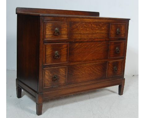 A 1930’s style oak chest of drawers of rectangular form with small gallery back atop two drawers and cupboard with drop front