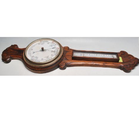 A 20th century carved oak Aneroid barometer and thermometer. The carved oak body with a removable thermometer section to top.