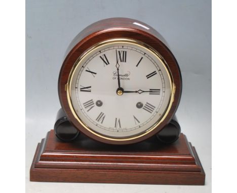 A Comitti of London mantel clock having a circular white enamel clock face with roman numerals to the chapter ring raised on 