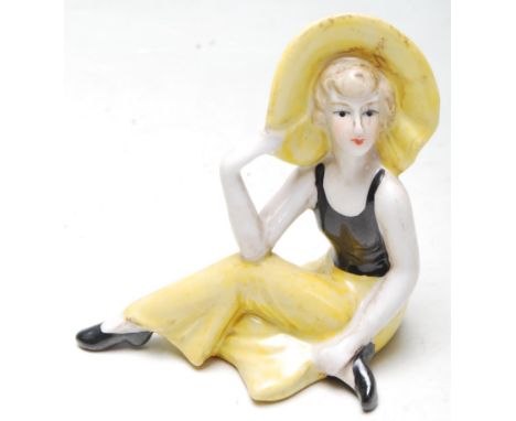 An Art Deco 1930s style ceramic figurine of a seated flapper girl wearing a canary yellow dress and hat. Stamped C280.