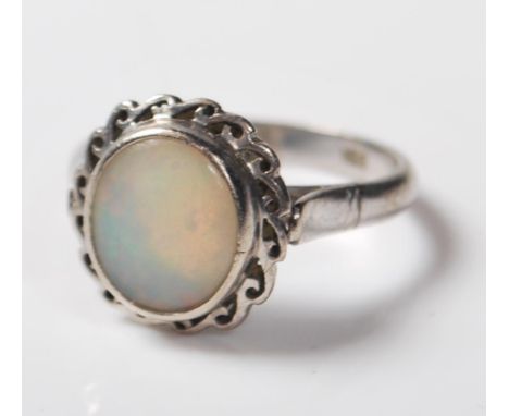 A 14ct white gold ring being bezel set with an oval opal cabochon with a decorative twist mount. Stamped 14k to the band. Wei