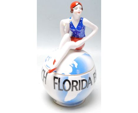 An Art Deco style ceramic lidded trinket bowl in the form of a globe with a 1930s polychrome flapper girl sat atop. Measures 