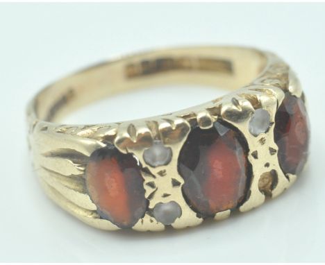 A 9ct gold ring having engraved foliate design shoulders with three large oval garnets and four small white stones( one is mi