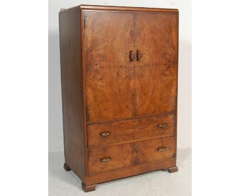 A 1930’s walnut pedestal wardrobe having twin doors over two long drawers with shaped handles raised on bracket feet.Measures