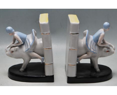 A pair of Art Deco 1930s style ceramic polychrome bookends of a flapper girl riding a pig exiting a book.&nbsp; Measures 15 h