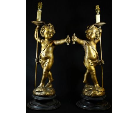 A pair of Continental giltwood figural lamps, of scantily clad amorini, each stands, an arrow in one hand, a sconce in the ot