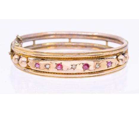 An early 20th century ruby and diamond set yellow metal bangle, comprising a row of alternate graduated round cut rubies set 