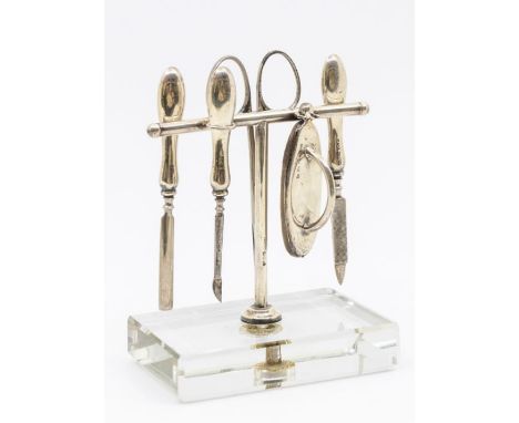 A novelty George V silver manicure set on glass base, to include; nail buffer, steel scissors and three nail files/tools. All