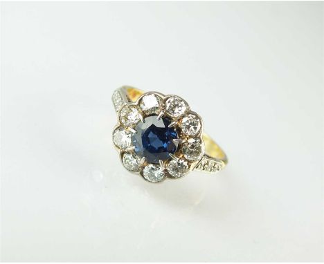 A sapphire and diamond floral cluster ring, designed as a central round mixed cut sapphire claw set within a border of nine b