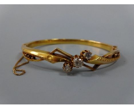 AN EARLY 20TH CENTURY DIAMOND BANGLE, with three graduated old-cut diamonds to a fancy-cut scrolling detailed bangle, to the 