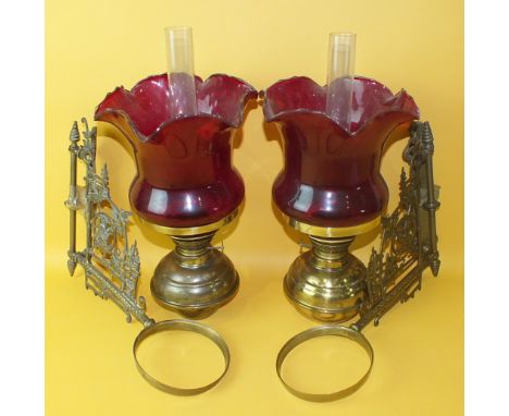 A pair of Edwardian brass bracket-mounted oil lamps with ruby glass shades, (2).
