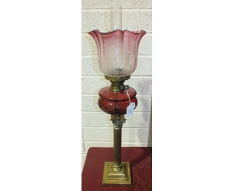 A Late-Victorian oil lamp, the cranberry glass reservoir on brass Corinthian column and square stepped base, with pink and cl