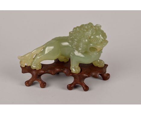 A Chinese carved hardstone Buddhist lion, the jade style green stone modelled as a rampant lion, presented on a carved wooden