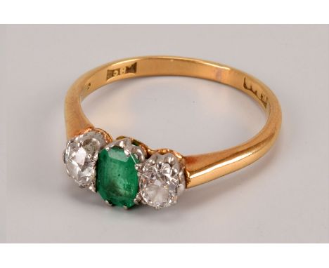 An Art Deco period three stone diamond and emerald ring, the 18ct gold mount having rectangular green central stone and a pai