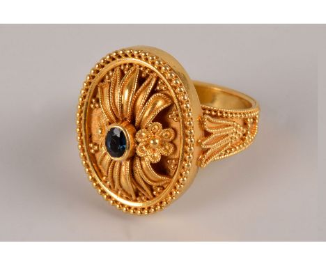 A modern Middle Eastern yellow metal dress ring, the ornate oval tablet with floral and leaf design and having rubbed over se