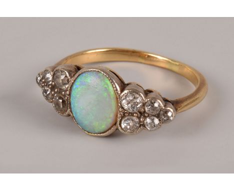 An Edwardian opal and diamond dress ring, the central oval opal in rubbed over setting having five graduating old cuts to eac