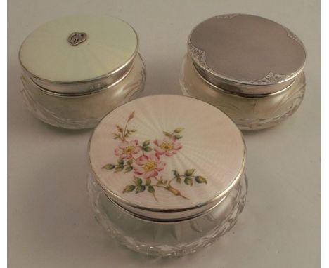 Two glass dressing table pots, with hallmarked silver covers, one decorated with enamel, together with another with silver pl