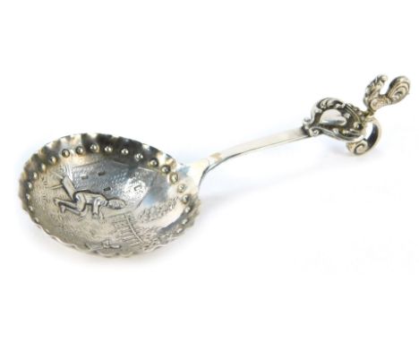 A Continental white metal caddy spoon, the bowl with a hammered edge and impressed beaded banding, decorated on an embossed s